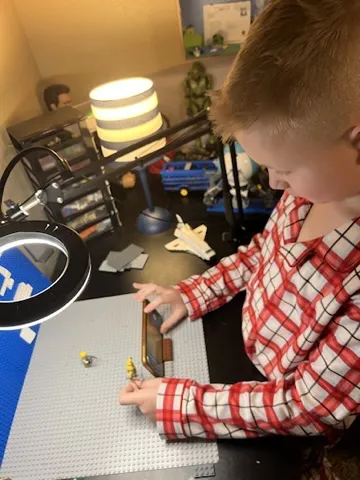 CJ moving minifigures on a baseplate in front of his phone